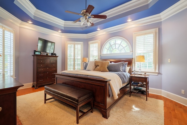 bedroom with wood finished floors, ornamental molding, ceiling fan, a raised ceiling, and baseboards