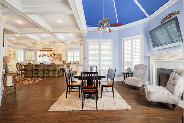 dining space with dark wood-style flooring, ceiling fan, crown molding, beamed ceiling, and a fireplace