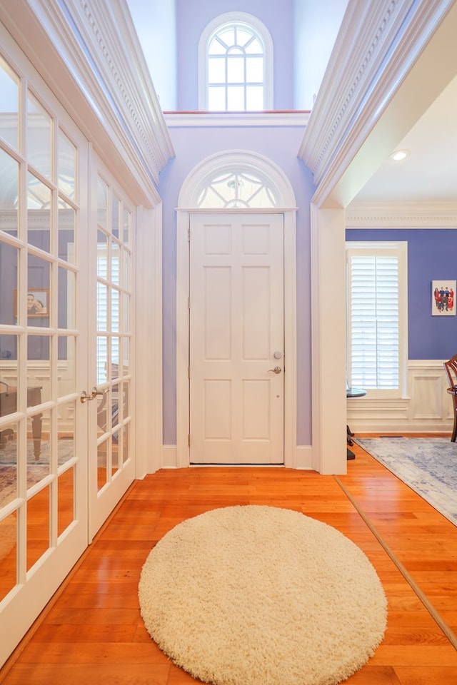 foyer with hardwood / wood-style floors, french doors, crown molding, and a wainscoted wall