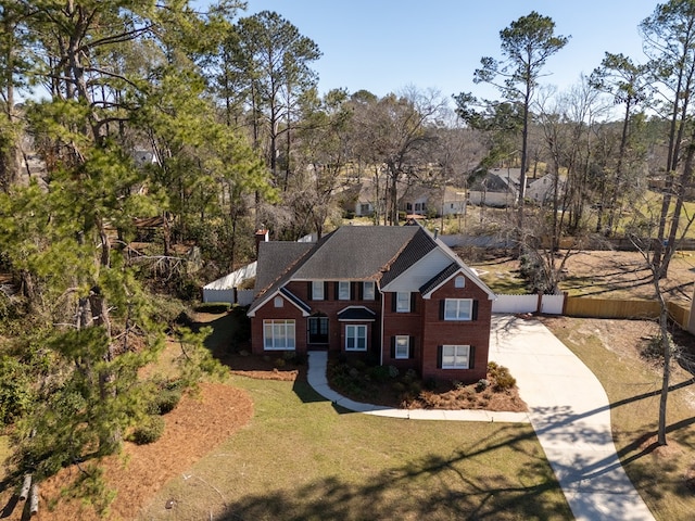 traditional home featuring brick siding, fence, driveway, a front lawn, and a chimney