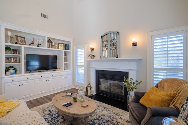 living area with a towering ceiling, a fireplace with flush hearth, visible vents, and wood finished floors