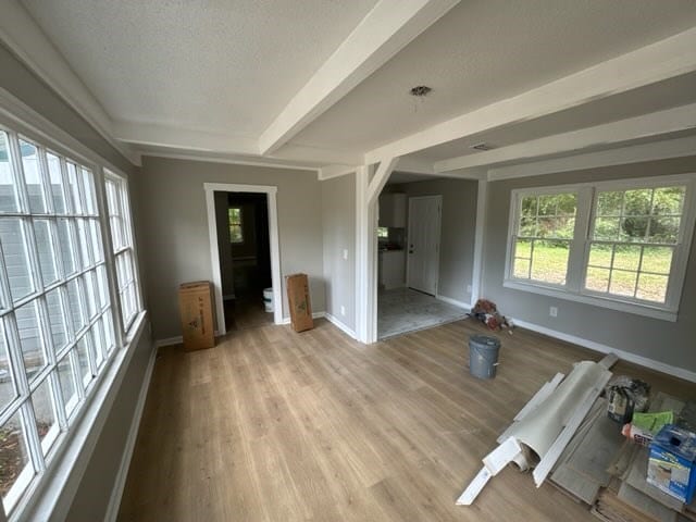 interior space with beam ceiling, a textured ceiling, and light hardwood / wood-style flooring