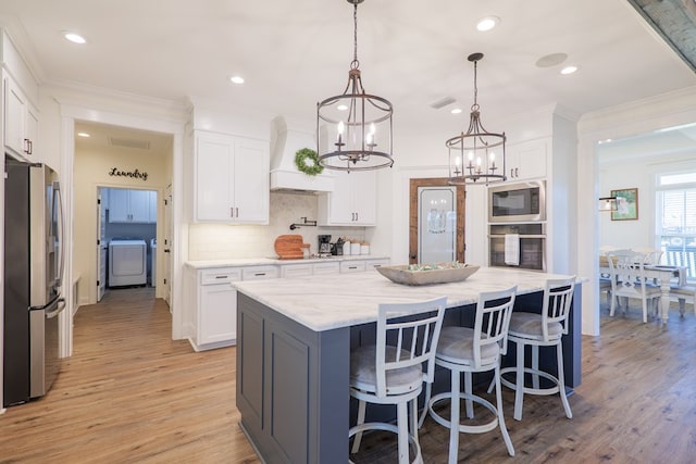 kitchen with white cabinets, pendant lighting, appliances with stainless steel finishes, and light hardwood / wood-style flooring