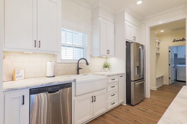 kitchen with appliances with stainless steel finishes, white cabinetry, washer / dryer, and sink