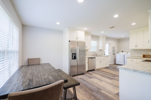 kitchen with white cabinets, sink, washing machine and dryer, light hardwood / wood-style floors, and stainless steel appliances