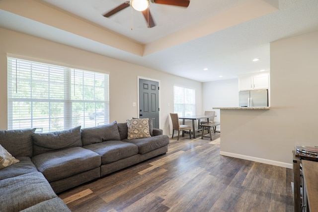 living room featuring dark hardwood / wood-style floors, a raised ceiling, and ceiling fan