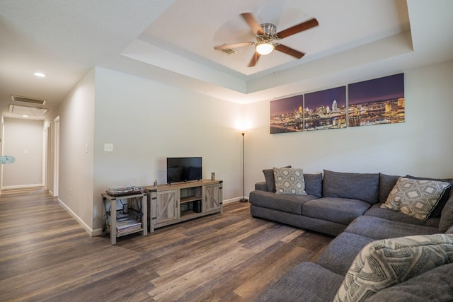 living room with a tray ceiling, ceiling fan, and dark hardwood / wood-style floors