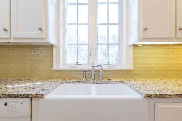 interior details with decorative backsplash, white cabinetry, a sink, and dishwashing machine