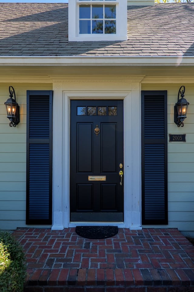 view of exterior entry featuring a porch and roof with shingles