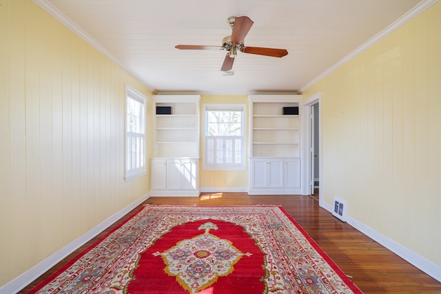spare room with built in shelves, wood finished floors, visible vents, baseboards, and ornamental molding
