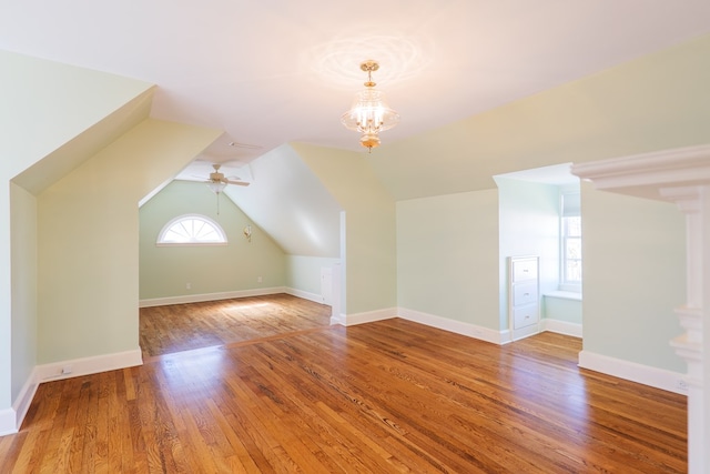 additional living space with ceiling fan with notable chandelier, vaulted ceiling, wood-type flooring, and baseboards