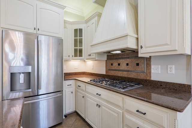 kitchen featuring tasteful backsplash, glass insert cabinets, white cabinetry, custom range hood, and appliances with stainless steel finishes