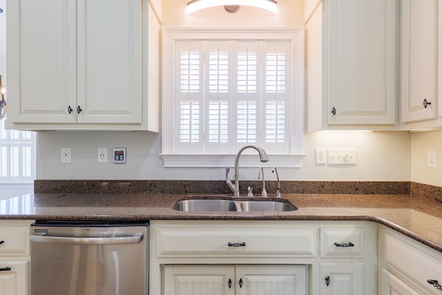 kitchen with white cabinets, stainless steel dishwasher, a sink, and dark stone counters