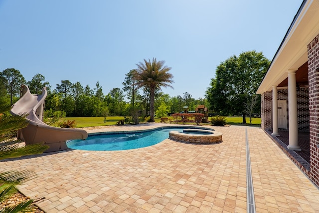 view of swimming pool featuring a pool with connected hot tub, a water slide, and a patio