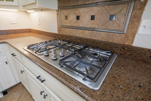 kitchen with decorative backsplash, stainless steel gas cooktop, white cabinetry, and light tile patterned floors