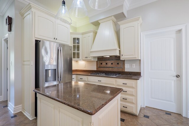 kitchen with stainless steel appliances, ornamental molding, premium range hood, dark stone counters, and glass insert cabinets