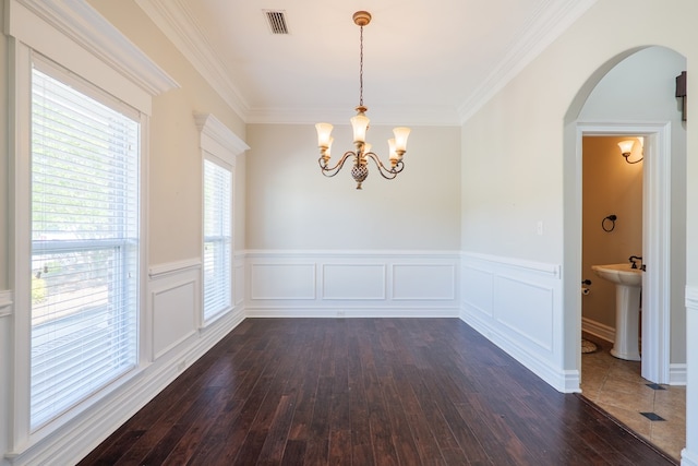 unfurnished dining area featuring arched walkways, a notable chandelier, a wainscoted wall, and dark wood-style flooring