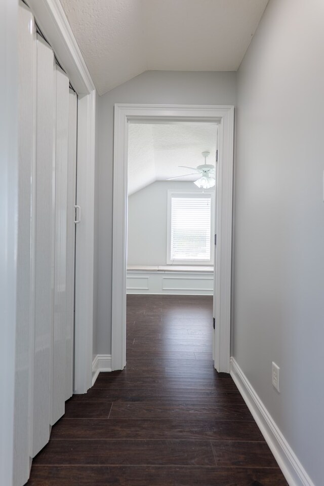 corridor featuring lofted ceiling, baseboards, and wood finished floors
