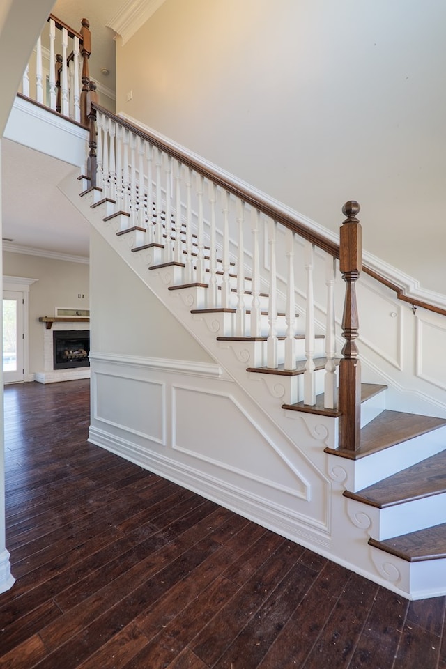 stairway featuring crown molding, hardwood / wood-style floors, and a fireplace with raised hearth