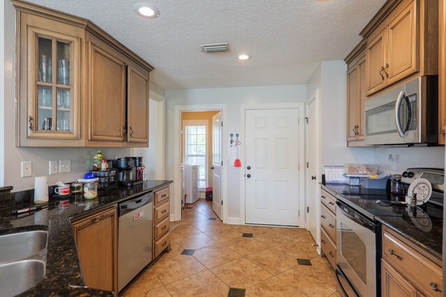 2783 Rabbit Ridge Run, Valdosta, GA 31605 - kitchen with stainless steel appliances, light tile patterned floors, glass insert cabinets, a textured ceiling, and dark stone counters
