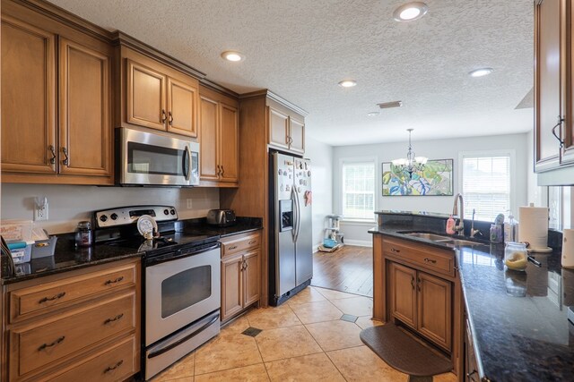 2783 Rabbit Ridge Run, Valdosta, GA 31605 - kitchen featuring appliances with stainless steel finishes, brown cabinets, a chandelier, light tile patterned floors, and dark stone counters