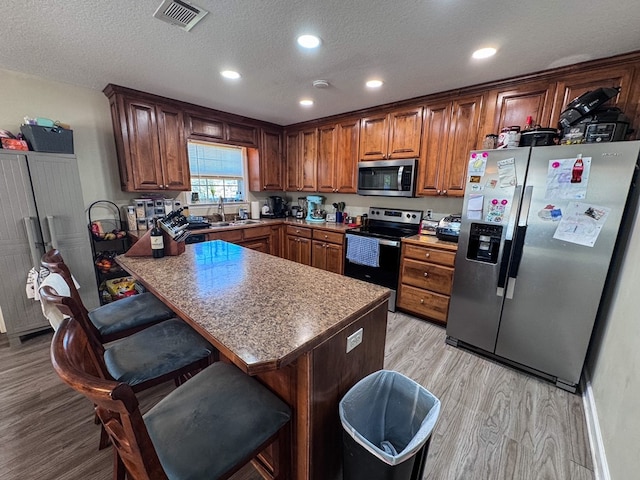 kitchen featuring visible vents, a kitchen breakfast bar, stainless steel appliances, light wood-type flooring, and a sink