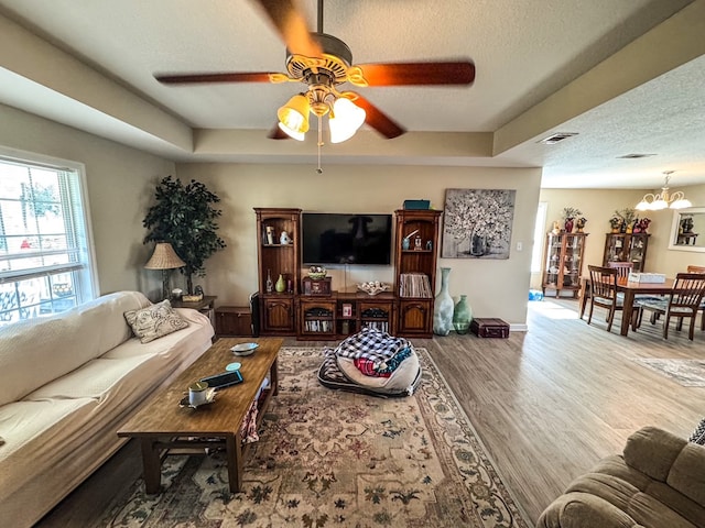 living room featuring a textured ceiling, a raised ceiling, wood finished floors, and ceiling fan with notable chandelier