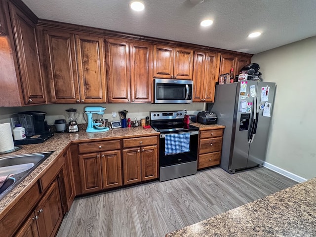 kitchen featuring a textured ceiling, a sink, light wood-style floors, appliances with stainless steel finishes, and brown cabinetry