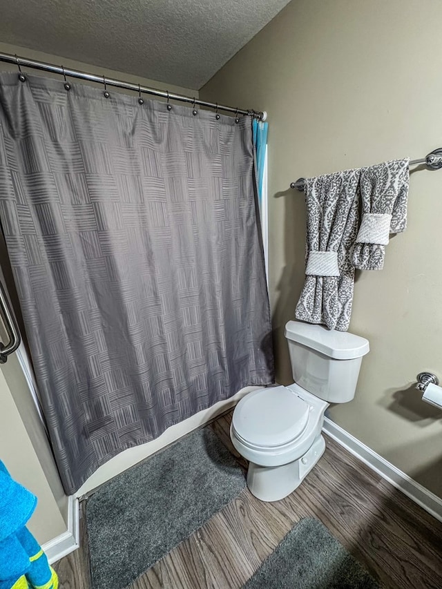 full bath featuring a textured ceiling, toilet, a shower with shower curtain, wood finished floors, and baseboards