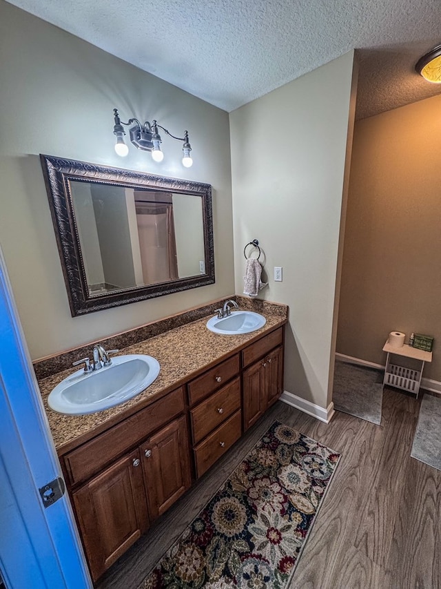 bathroom with double vanity, a sink, a textured ceiling, and wood finished floors