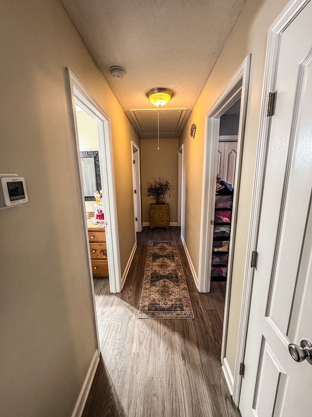 hallway with attic access, dark wood-type flooring, a textured ceiling, and baseboards