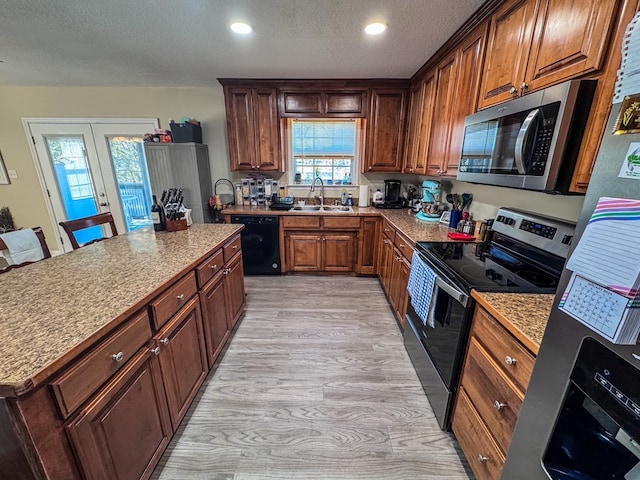 kitchen with light wood-style flooring, appliances with stainless steel finishes, a textured ceiling, french doors, and a sink