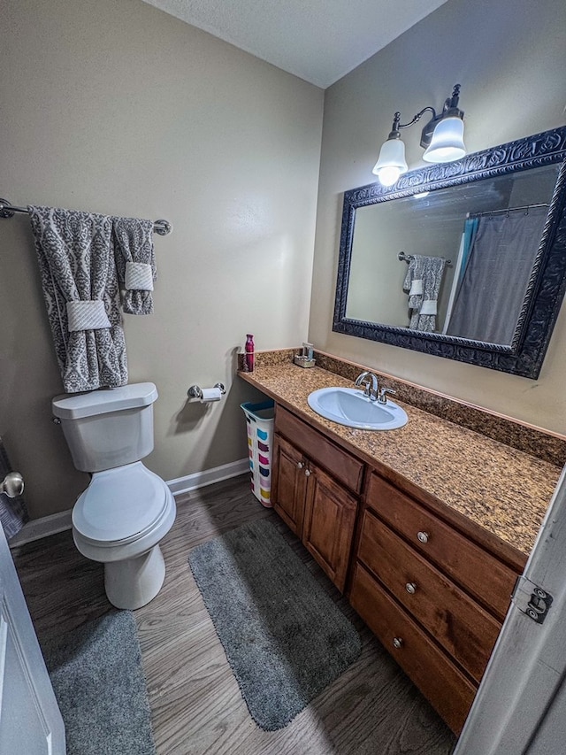 bathroom featuring baseboards, vanity, toilet, and wood finished floors