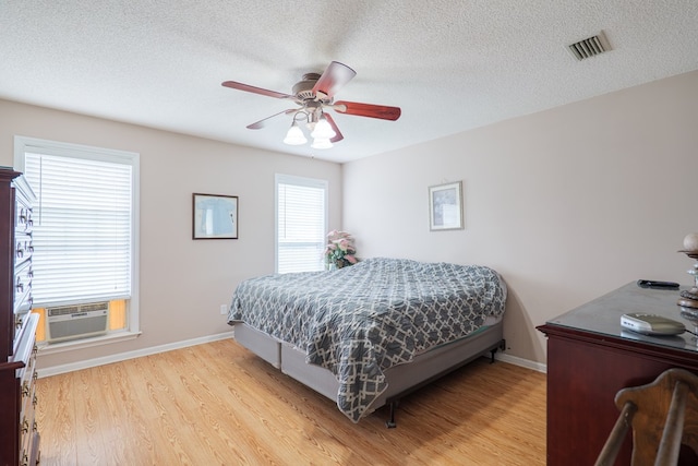 bedroom featuring a textured ceiling, cooling unit, visible vents, and light wood-style floors