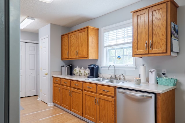 kitchen featuring stainless steel dishwasher, light countertops, a sink, and light wood-style floors