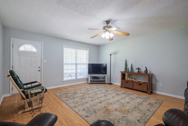 living area featuring a textured ceiling, ceiling fan, baseboards, and wood finished floors