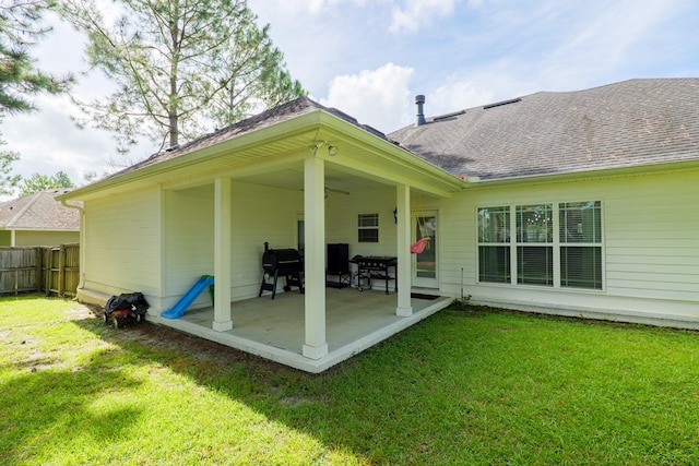 rear view of property featuring a lawn, fence, a shingled roof, ceiling fan, and a patio area