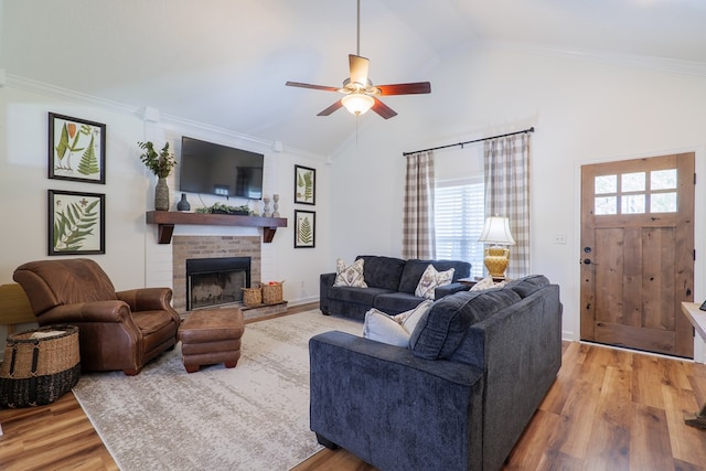 living area with ceiling fan, ornamental molding, a fireplace, wood finished floors, and high vaulted ceiling