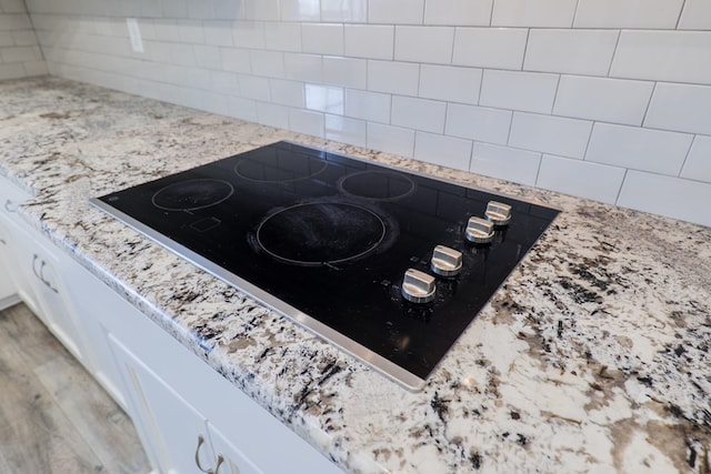 interior details featuring white cabinetry, black electric stovetop, decorative backsplash, and wood-type flooring