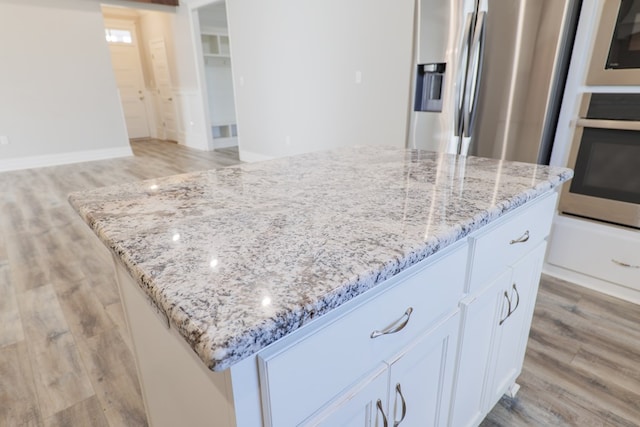 kitchen featuring a center island, light hardwood / wood-style flooring, stainless steel appliances, light stone countertops, and white cabinets