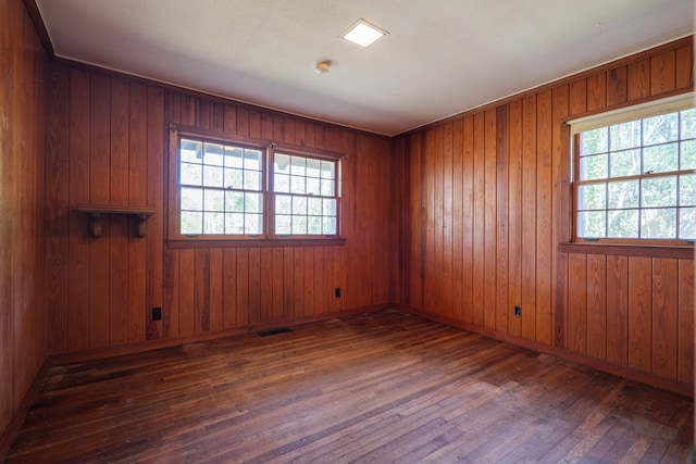 spare room featuring wood walls, dark hardwood / wood-style floors, and a healthy amount of sunlight