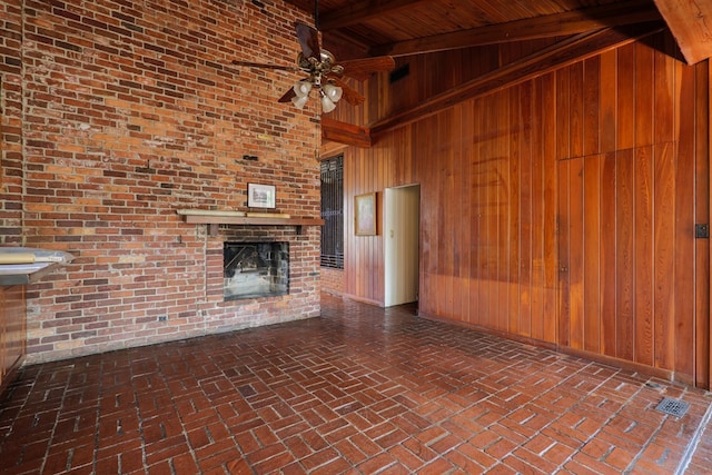 unfurnished living room featuring a brick fireplace, a towering ceiling, ceiling fan, wooden walls, and beam ceiling