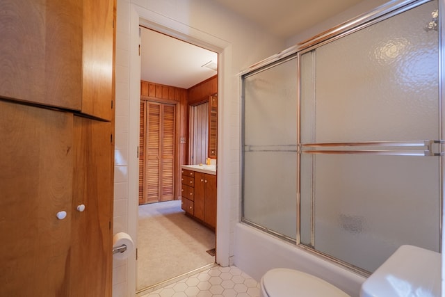 full bathroom featuring wooden walls, toilet, vanity, and bath / shower combo with glass door