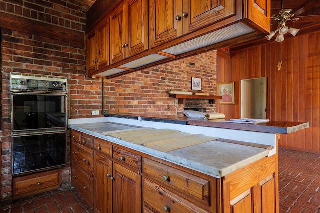 kitchen featuring ceiling fan, wood walls, and double oven