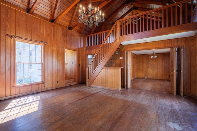 unfurnished living room featuring hardwood / wood-style flooring, beamed ceiling, a chandelier, and wooden walls