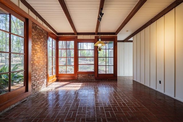 unfurnished sunroom featuring rail lighting, a healthy amount of sunlight, and beam ceiling