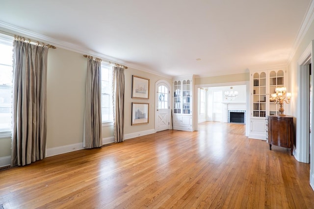 unfurnished living room with ornamental molding, light wood-type flooring, a notable chandelier, and a brick fireplace