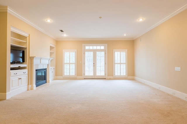 unfurnished living room featuring built in shelves, light colored carpet, crown molding, and french doors