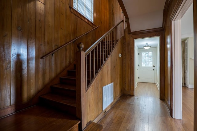 staircase with hardwood / wood-style floors, wood walls, and crown molding