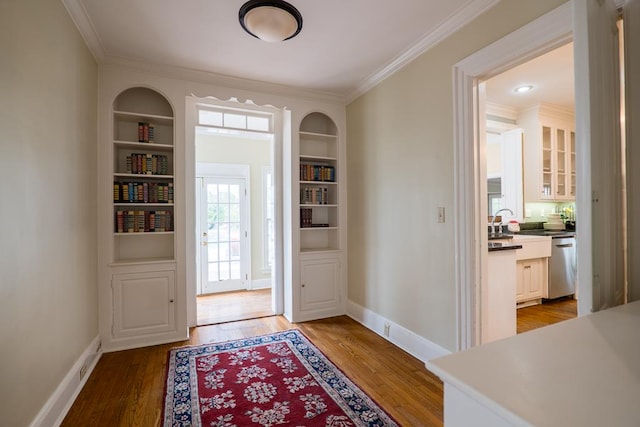 doorway to outside with built in shelves, crown molding, and light hardwood / wood-style flooring